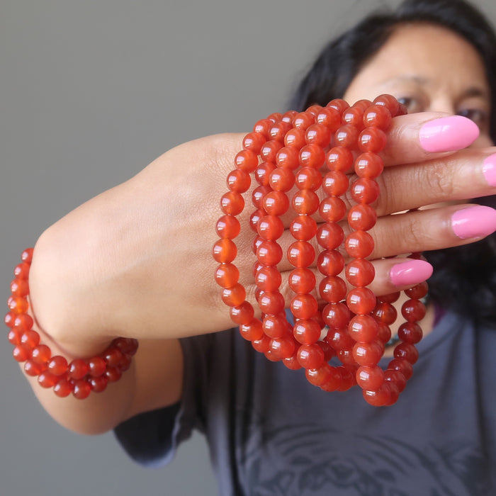 sheila of satin crystals holding a stack of carnelian bracelets