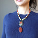sheila of satin crystals wearing Necklace made of Carnelian Serpentine and brass beads with oval carnelian hanging underneath painted peacock on brass pendant 