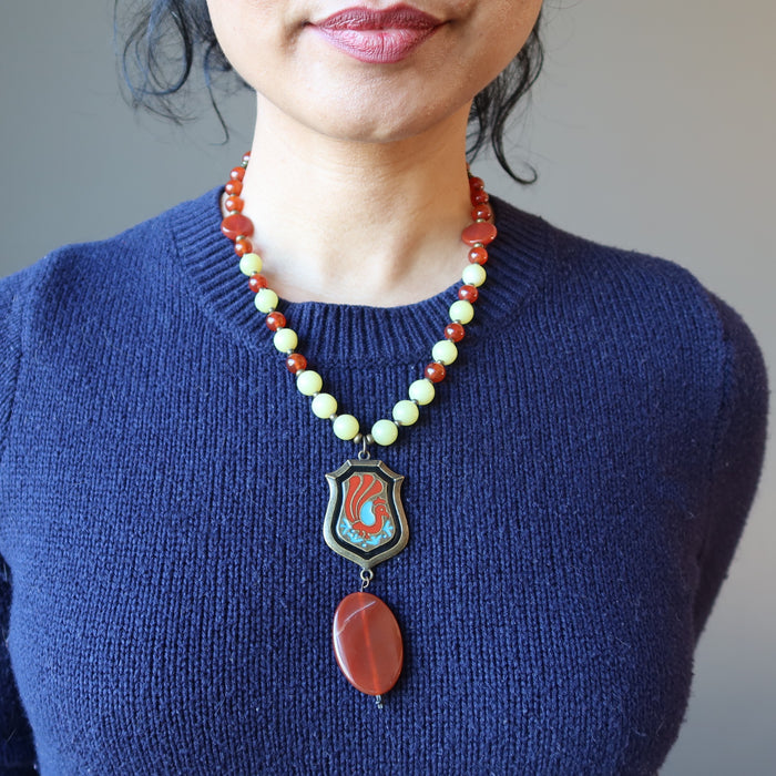 sheila of satin crystals wearing Necklace made of Carnelian Serpentine and brass beads with oval carnelian hanging underneath painted peacock on brass pendant 