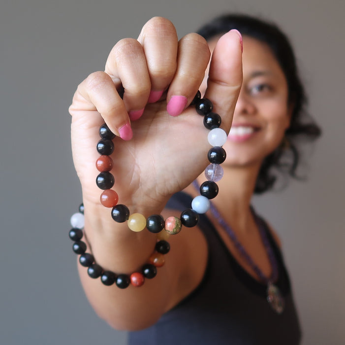 sheila of satin crystals holding out a rainbow obsidian and natural chakra stone stretch bracelet beaded with round gemstones