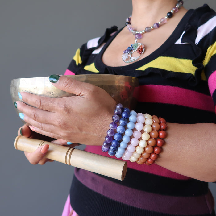 sheila of satin crystals wearing set of 7 chakra bracelets with amethyst, sodalite, angelite, rose quartz, calcite, aventurine and red jasper holding a tibetan singing bowl