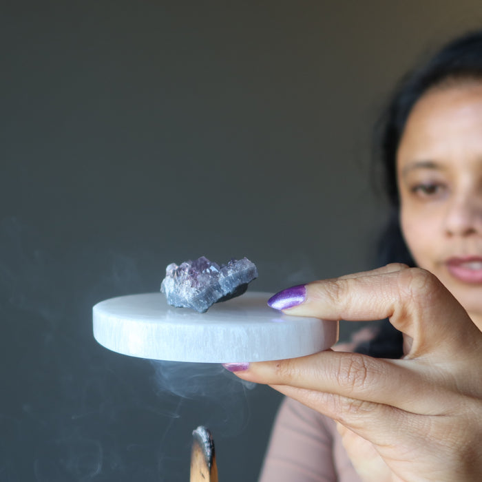 woman smoking palo santo under selenite slab with amethyst clutser