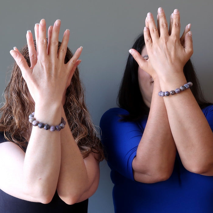 two female models with hands up in front of their faces both wearing charoite bracelets