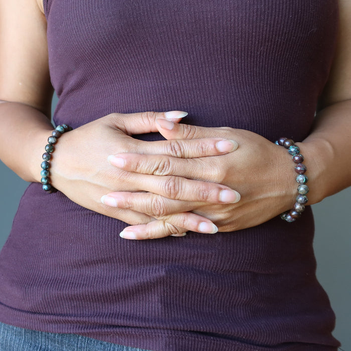 female hands clasped at stomach wearing chrysocolla cuprite bracelets in each wrist
