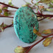 blue-green and black chrysocolla oval cabochon leaning on flower branches