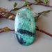 hand holding blue-green and black chrysocolla oval cabochon leaning against flower branches