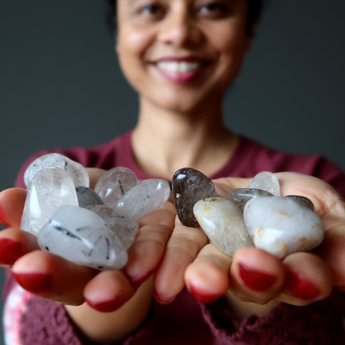 woman holding tourmaline and rutilated quartz tumbled stones in hands