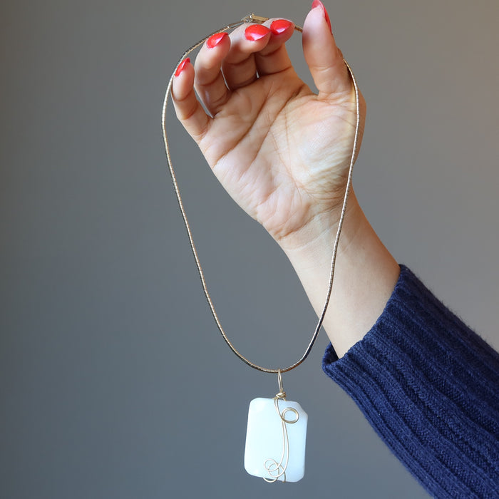 hand holding wavy rectangle white Dolomite stone wrapped in gold plated wire pendant hangs on Gold plated choker