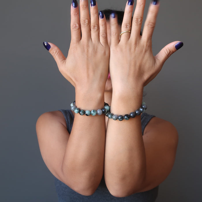 female model with hands up wearing two emerald stretch bracelets