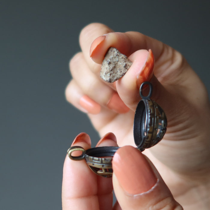 hand putting gao-guenie meteorite in locket pendant