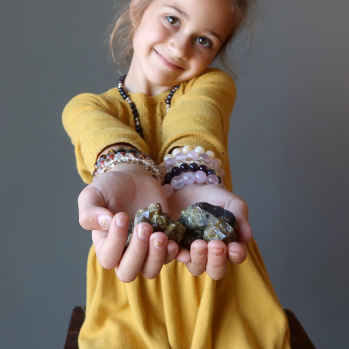 female child holding out raw green garnets