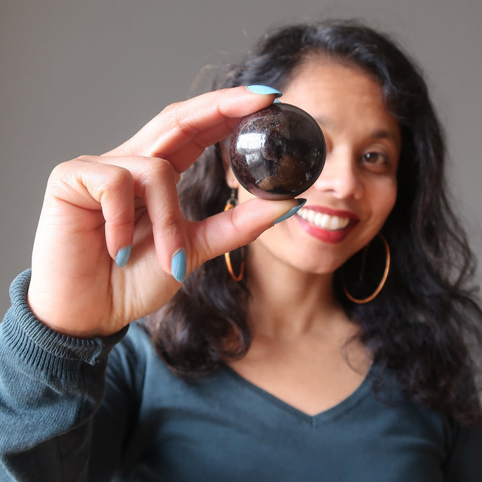sheila of satin crystals holding up a dark red garnet sphere in front of her eye
