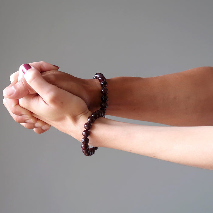 man and woman holding hands wearing red garnet bracelets