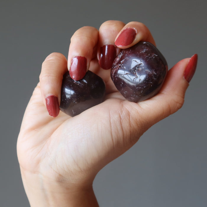 hand holding a pair of red garnet tumbled stones