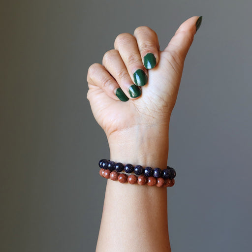 female hand making a thumbs up wearing blue and brown goldstone bracelet set