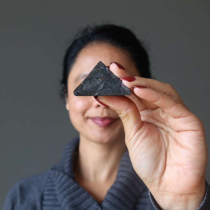 hand holding hematite pyramid in front of face