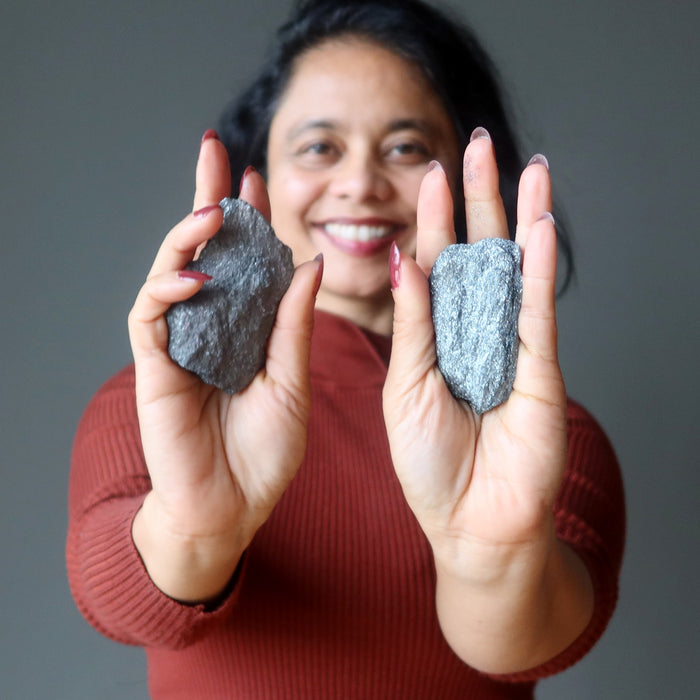 woman holding two raw specular hematite stones