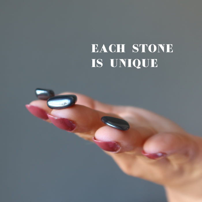 three finger tips holding Hematite Tumbled Stones on the hand