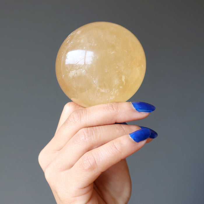 hand holding a honey calcite sphere