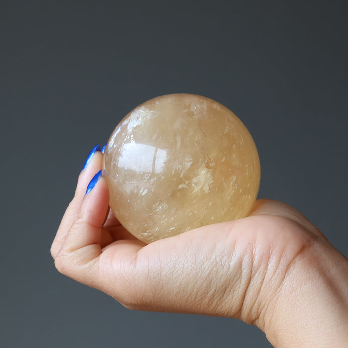 hand holding a honey calcite sphere