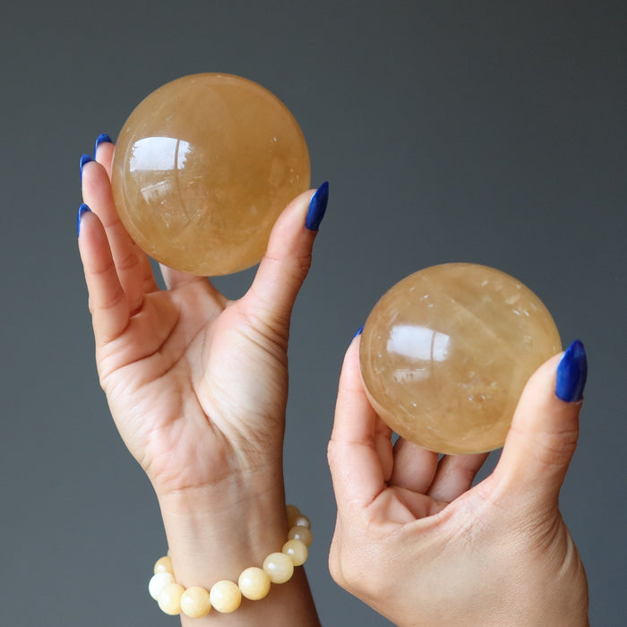 hands holding up two honey calcite spheres