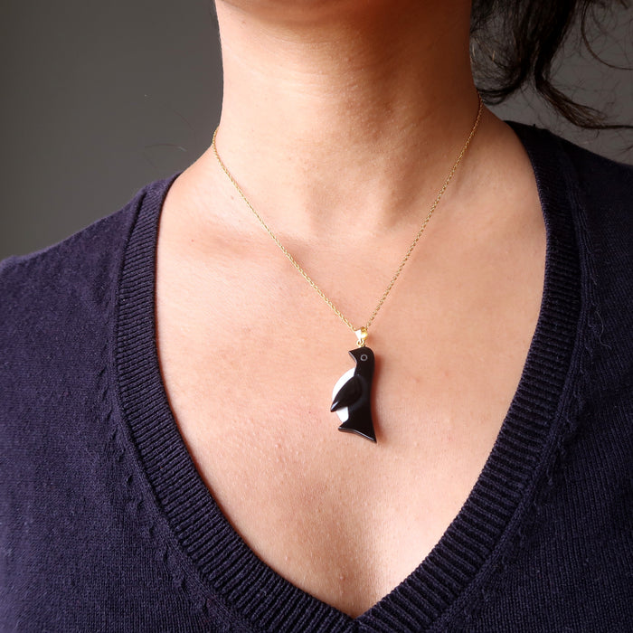 a model wearing black onyx and white howlite penguin pendant on 14 karat gold necklace chain