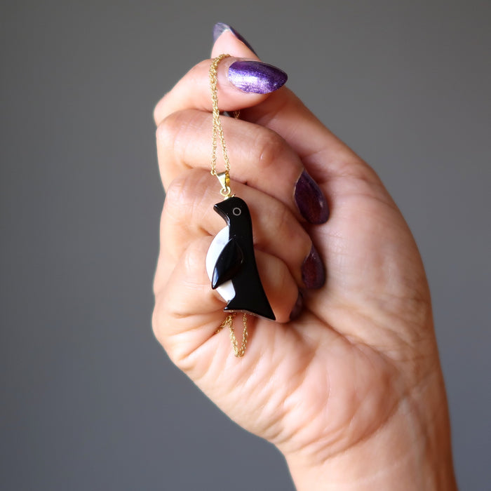 hand holding black onyx and white howlite penguin pendant on 14 karat gold necklace chain