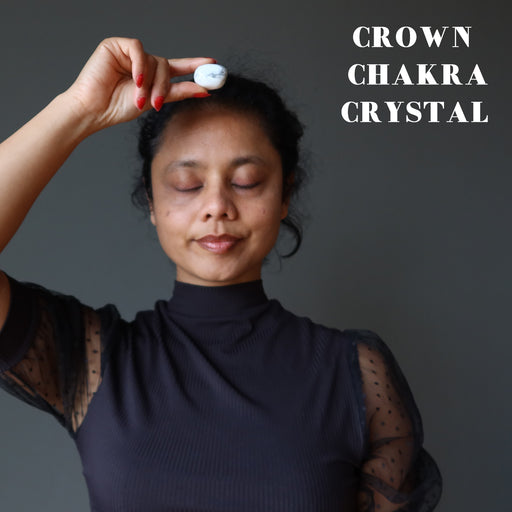 sheila of satin crystals holding white and gray howlite tumbled stone at her crown chakra