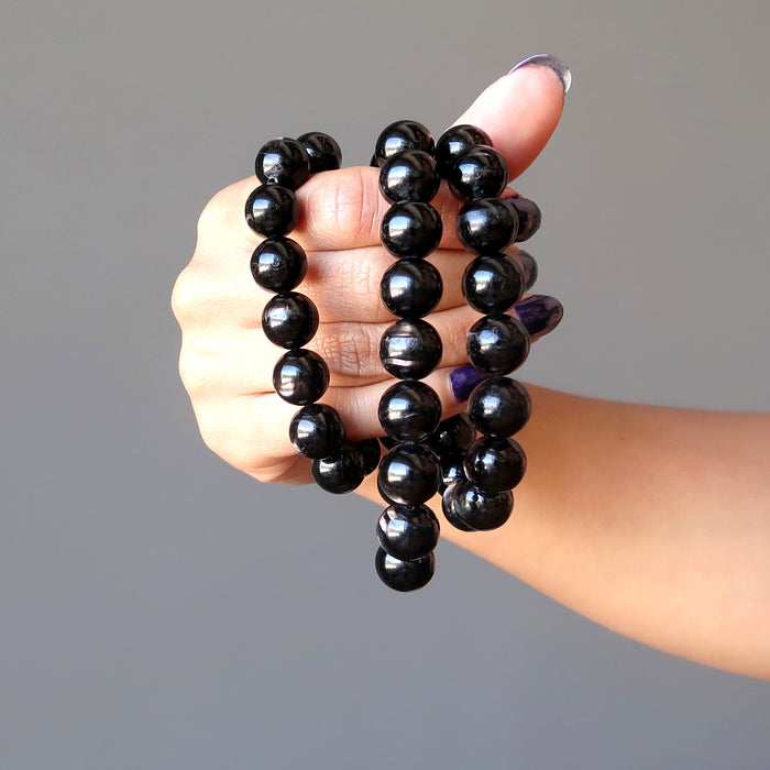 female hand holding 3 hypersthene bracelets