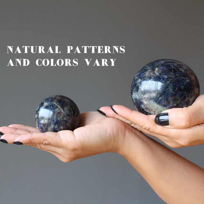 two hands holding iolite spheres in each palm showing natural patterns and colors vary