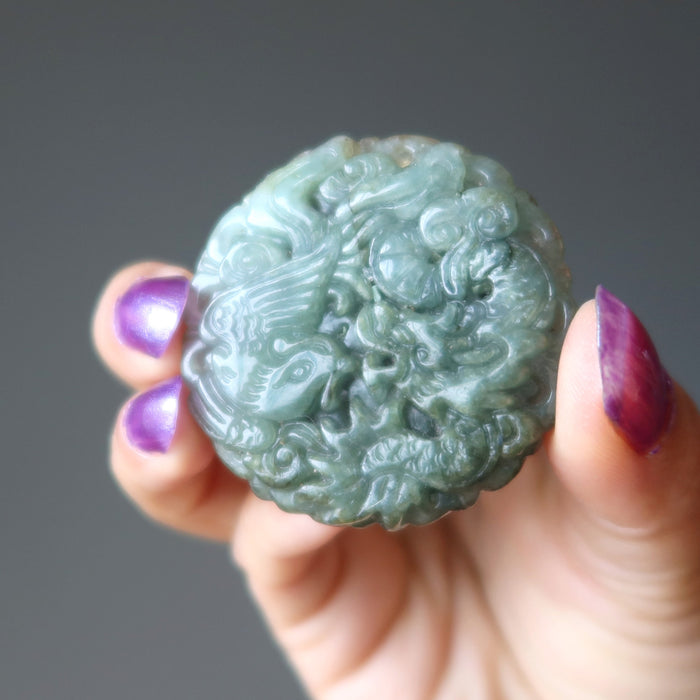 hand holding green jadeite amulet carved with dragon and phoenix