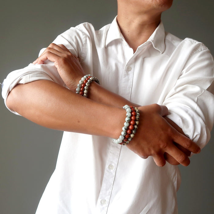 man with arms crossed wearing set of 3 sesame, red and dalmatian jasper stretch bracelets on each hand.
