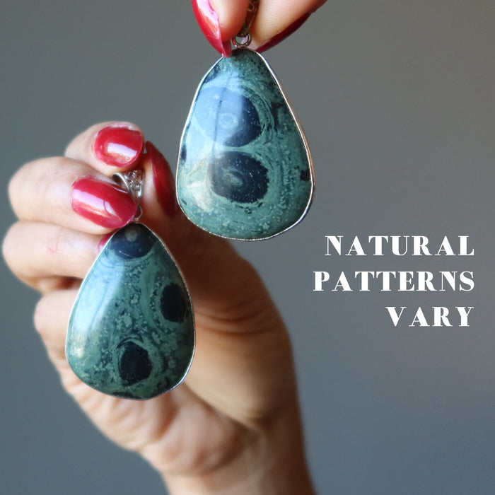 hand holding 2 kambaba jasper pendants to show natural patterns vary