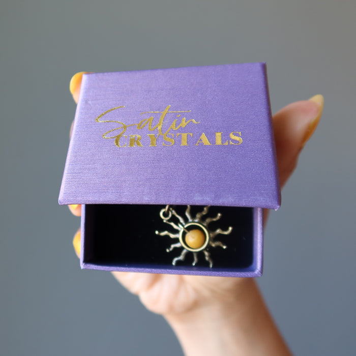 hand holding yellow jasper sun pendant in satin crystals gift box