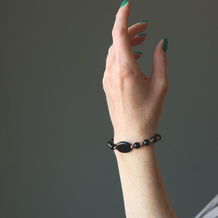 female hand raised wearing black jet stone and copper beaded bracelets