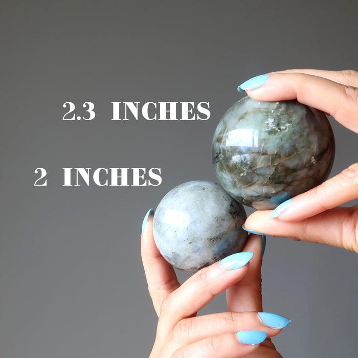 hand holding two labradorite spheres to compare size
