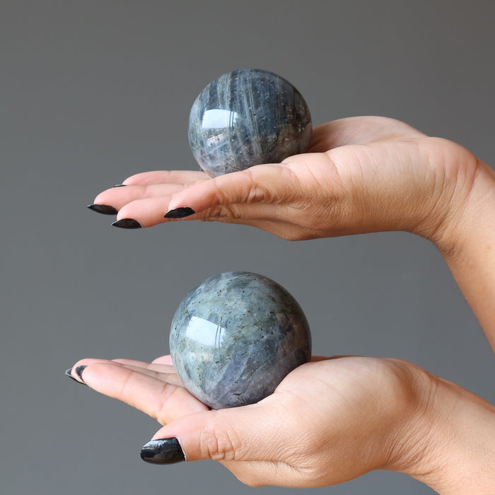 two hands each holding labradorite spheres in the palms