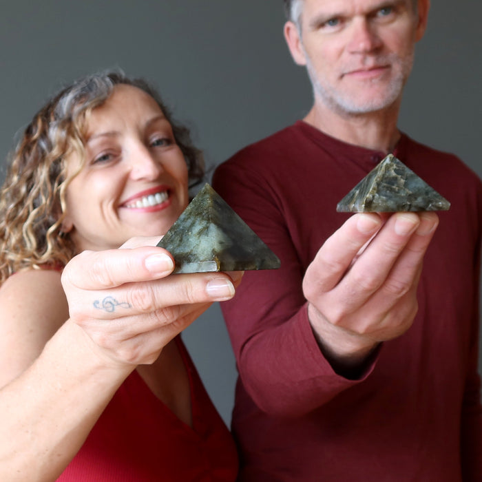 man and woman holding labradorite pyramids