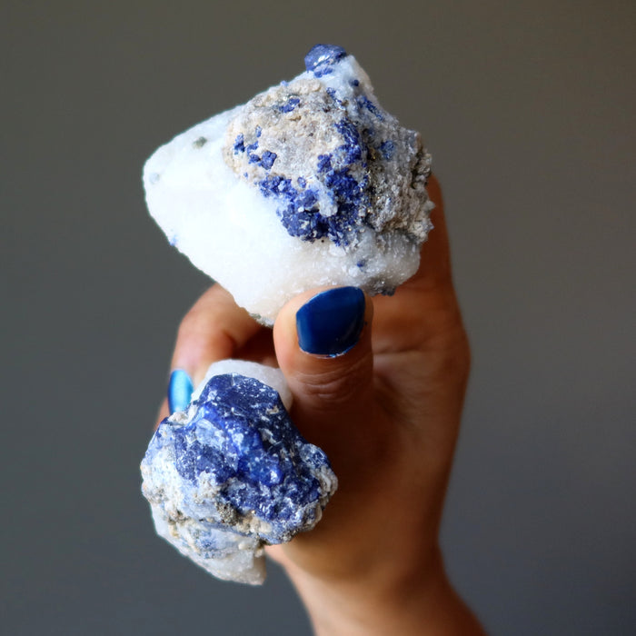 hand holding pair of blue lazurite and gold pyrite on white calcite raw minerals