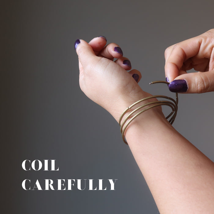 hand coiling red lava coil bracelet on a wrist with a sign saying "coil carefully"