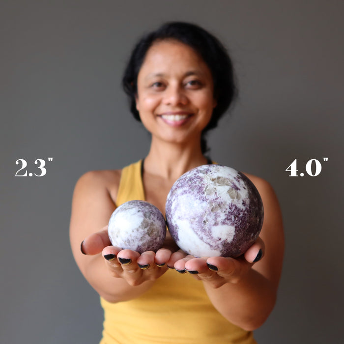 sheila of satin crystals holding two lepidolite spheres to show size difference
