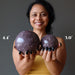 sheila of satin crystals holding two purple lepidolite spheres to show size difference