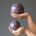 pair of hands holding purple lepidolite spheres in each palm