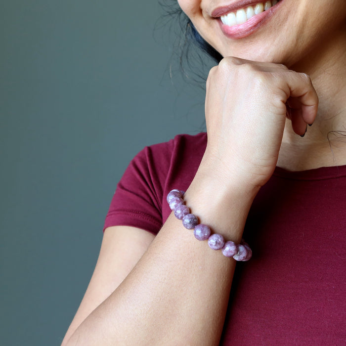 Sheila of Satin Crystals holds her wrist to her chin while showcasing the purple lepidolite bracelet and smiling