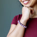 Sheila of Satin Crystals holds her wrist to her chin while showcasing the purple lepidolite bracelet and smiling