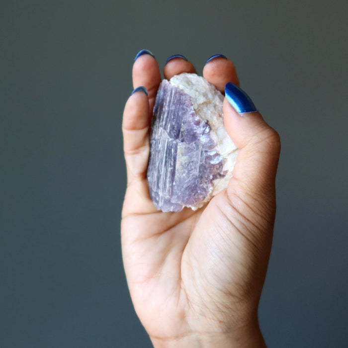 hand holding rough purple lepidolite on white quartz cluster