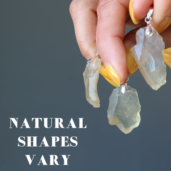 hand holding three libyan desert glass pendants to show natural shapes vary