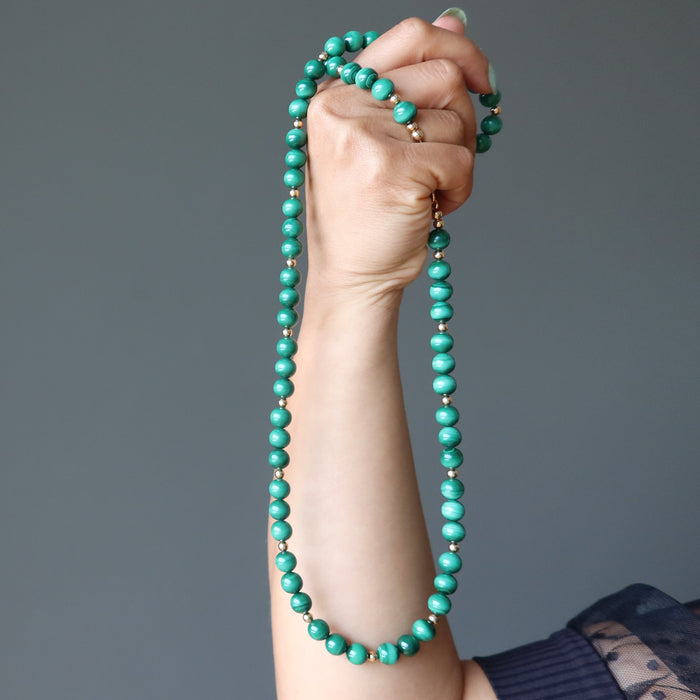 hand holding green malachite necklace with gold accent beads