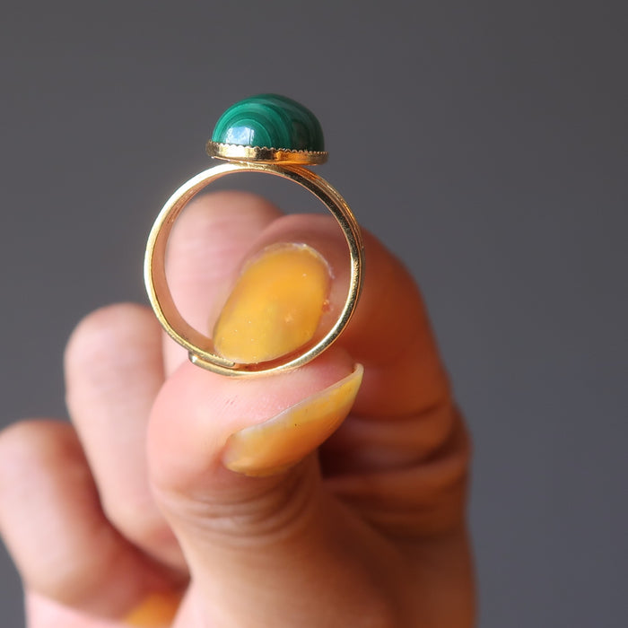 hand holding green oval malachite in gold adjustable ring