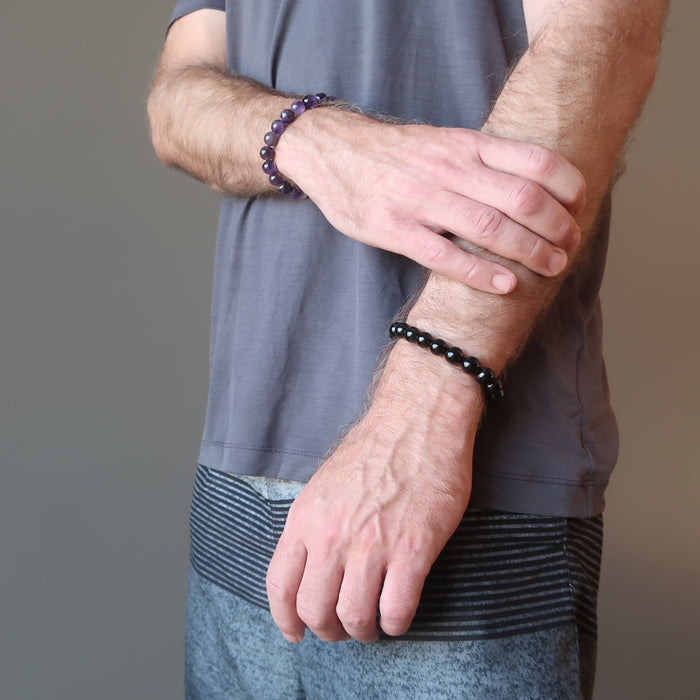 man wearing amethyst bracelet on one wrist and black tourmaline bracelet on the other